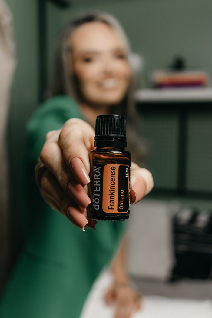 Close-up of a woman holding a frankincense essential oil bottle, focusing on her manicured nails.