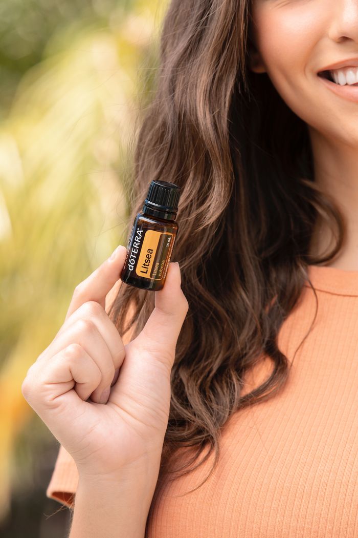 Woman holding a litsea essential oil bottle outdoors with a blurred natural background.