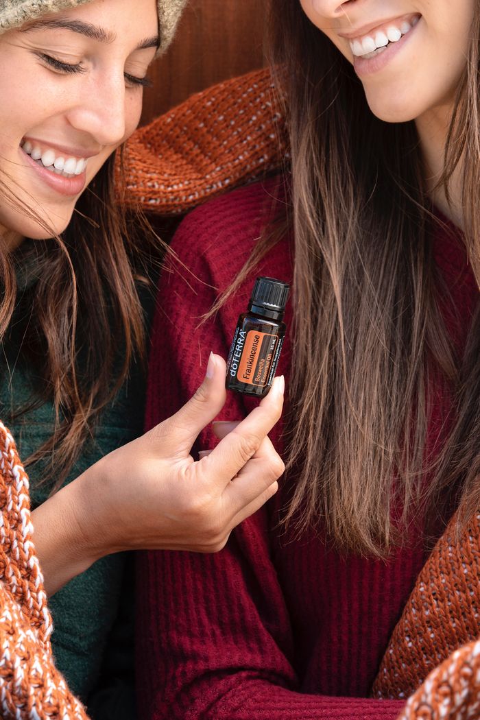 Two women happily sharing essential oils for aromatherapy indoors, capturing a moment of well-being and friendship.
