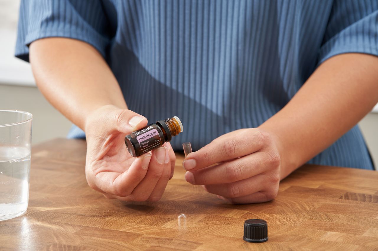 Close-up of hands pouring doterra essential oil into a glass, showcasing wellness and aromatherapy.